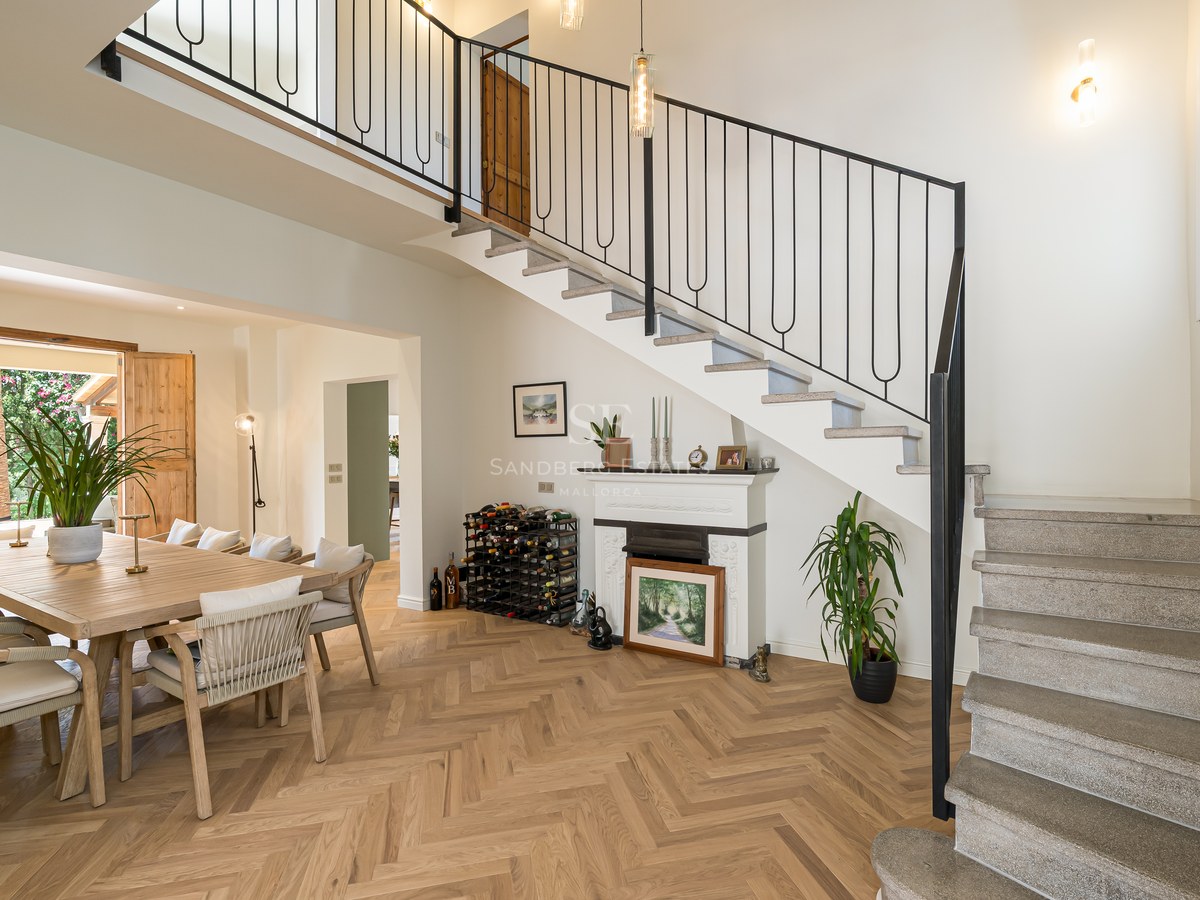 Dining area featuring an oak table, herringbone wood flooring, and a stone staircase with iron railings.