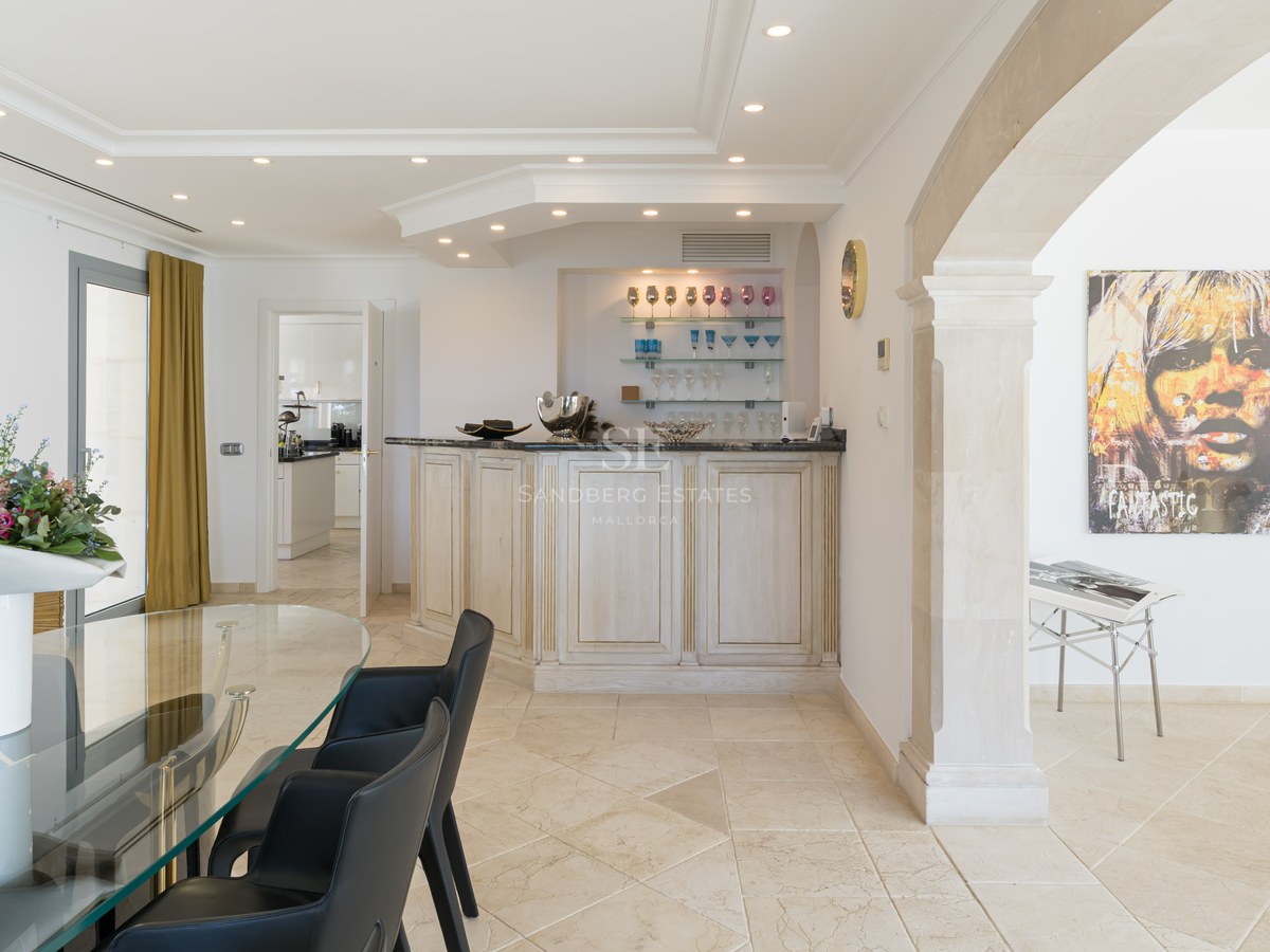 Modern dining room featuring a glass table, dark chairs, a white service bar, and a classical stone archway.