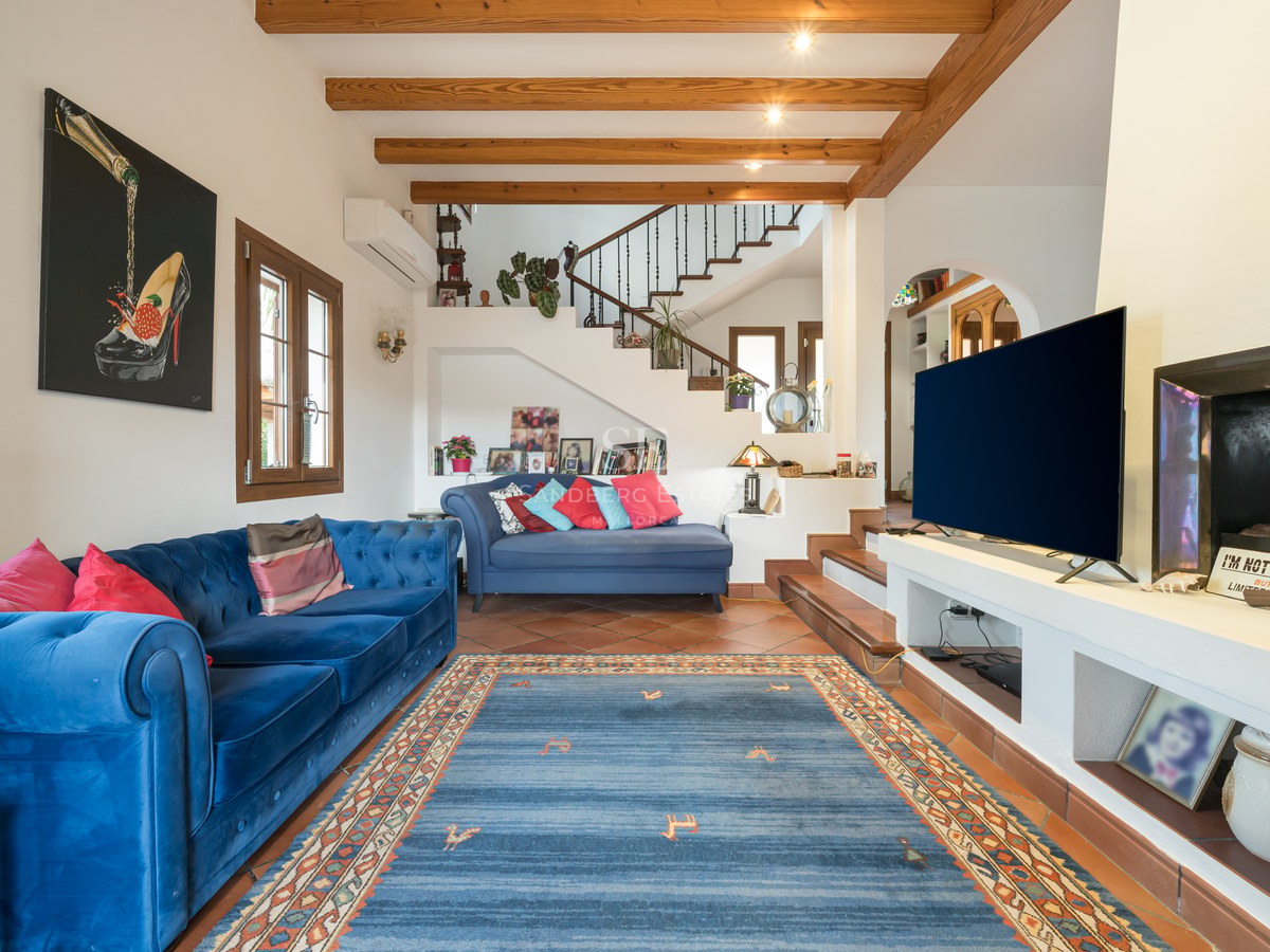 Salon spacieux avec canapés en velours bleu, poutres en bois apparentes au plafond et sol en terre cuite traditionnelle.