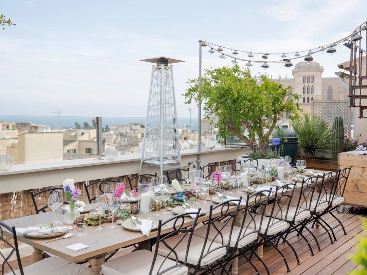 An elegantly set dining table on a wooden deck terrace overlooking a historic city and the sea.
