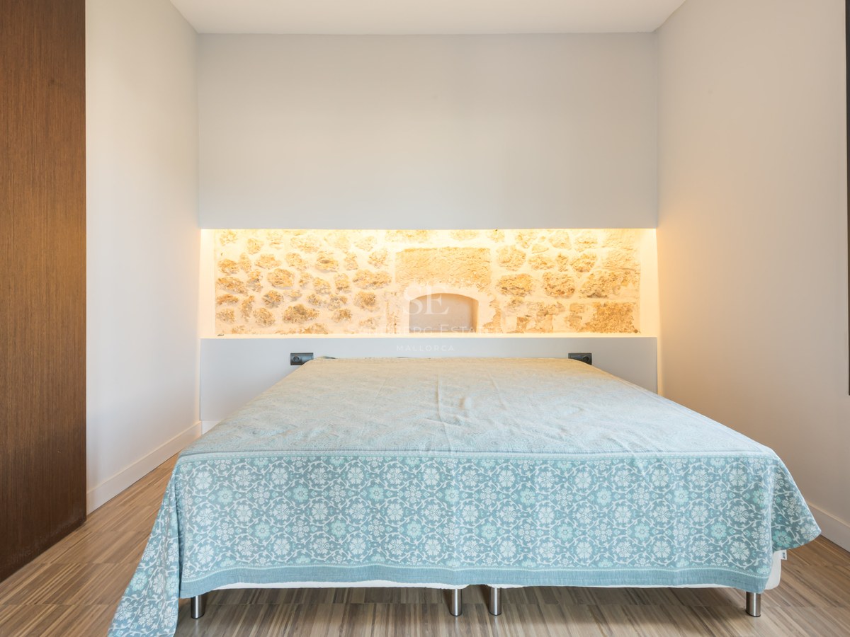 Modern bedroom featuring a bed, an illuminated natural stone wall niche, and light wood flooring.