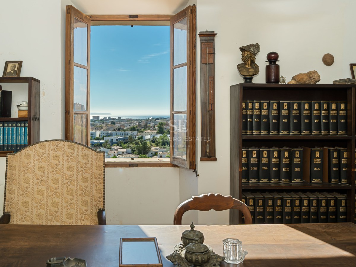 Estudio tradicional con escritorio de madera y ventana abierta con vistas a una ciudad costera y al mar.