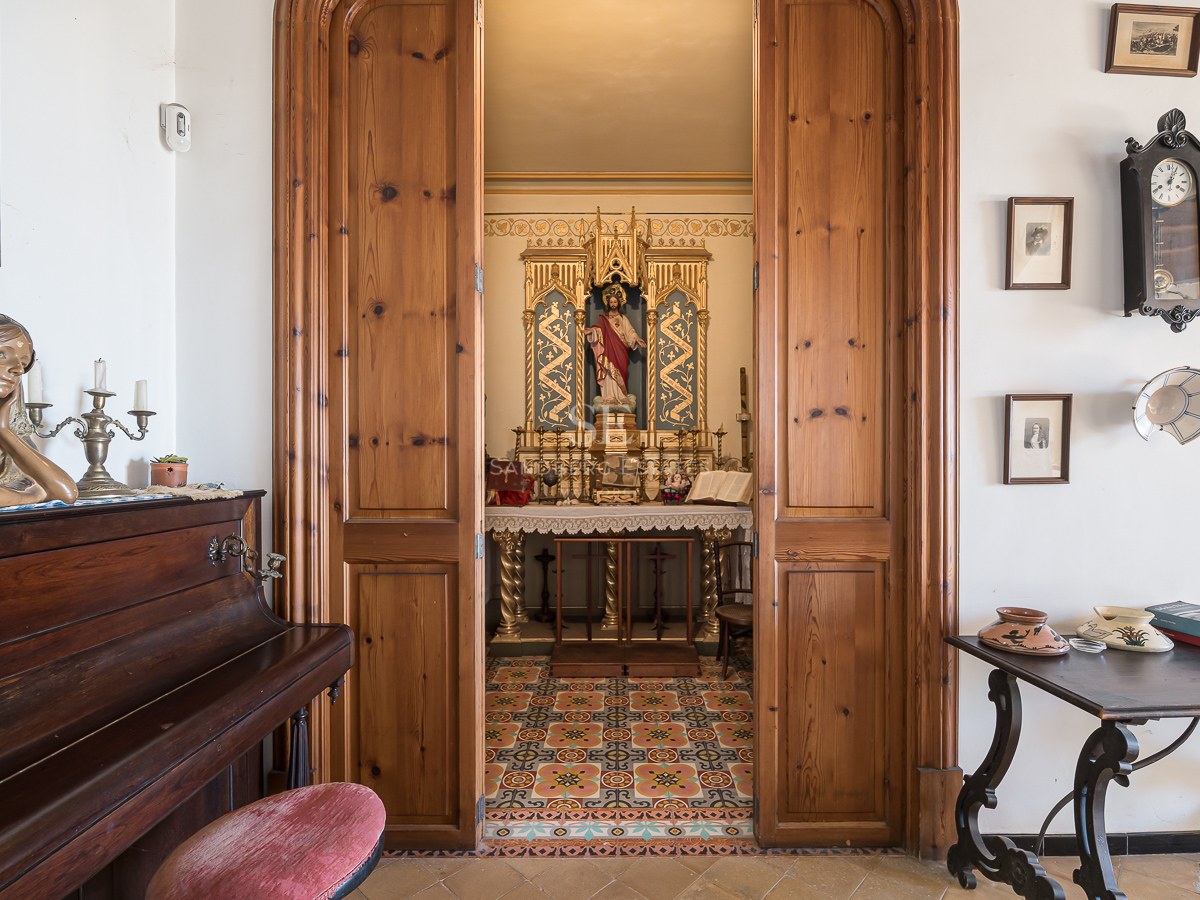 Vista a través de puertas de madera hacia una pequeña capilla privada ornamentada junto a un piano vertical.