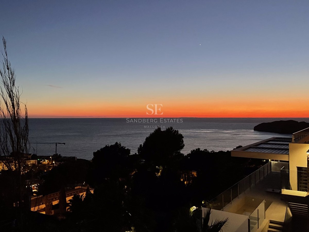 Coucher de soleil sur la mer depuis la terrasse d'une villa moderne avec balustrades en verre et éclairage nocturne.