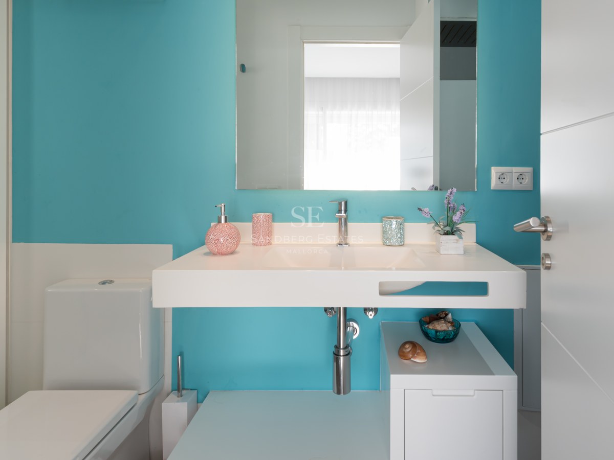 Modern bathroom with a vibrant turquoise wall, floating white sink, large mirror, and white toilet.