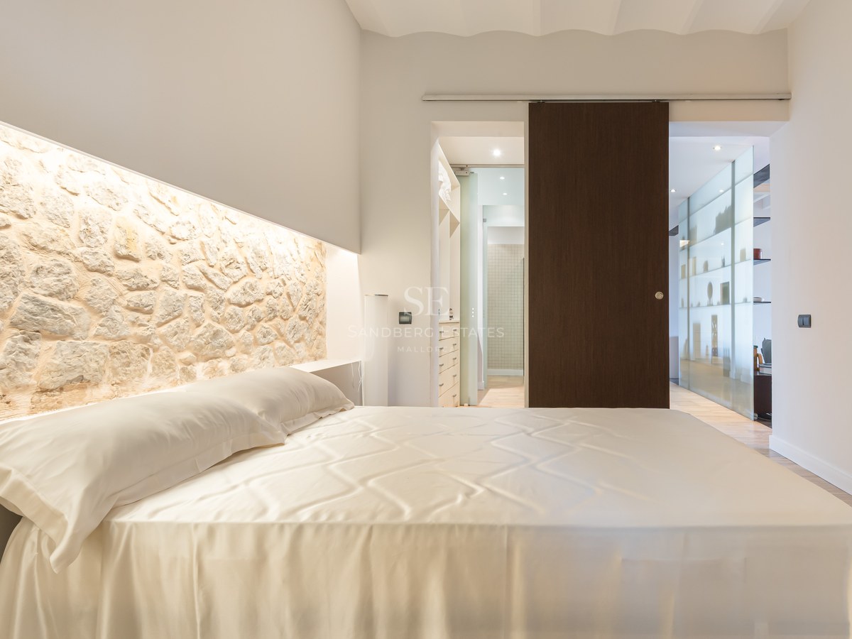 Luxury bedroom featuring a large bed, an illuminated natural stone headboard wall, and a dark wood sliding door.