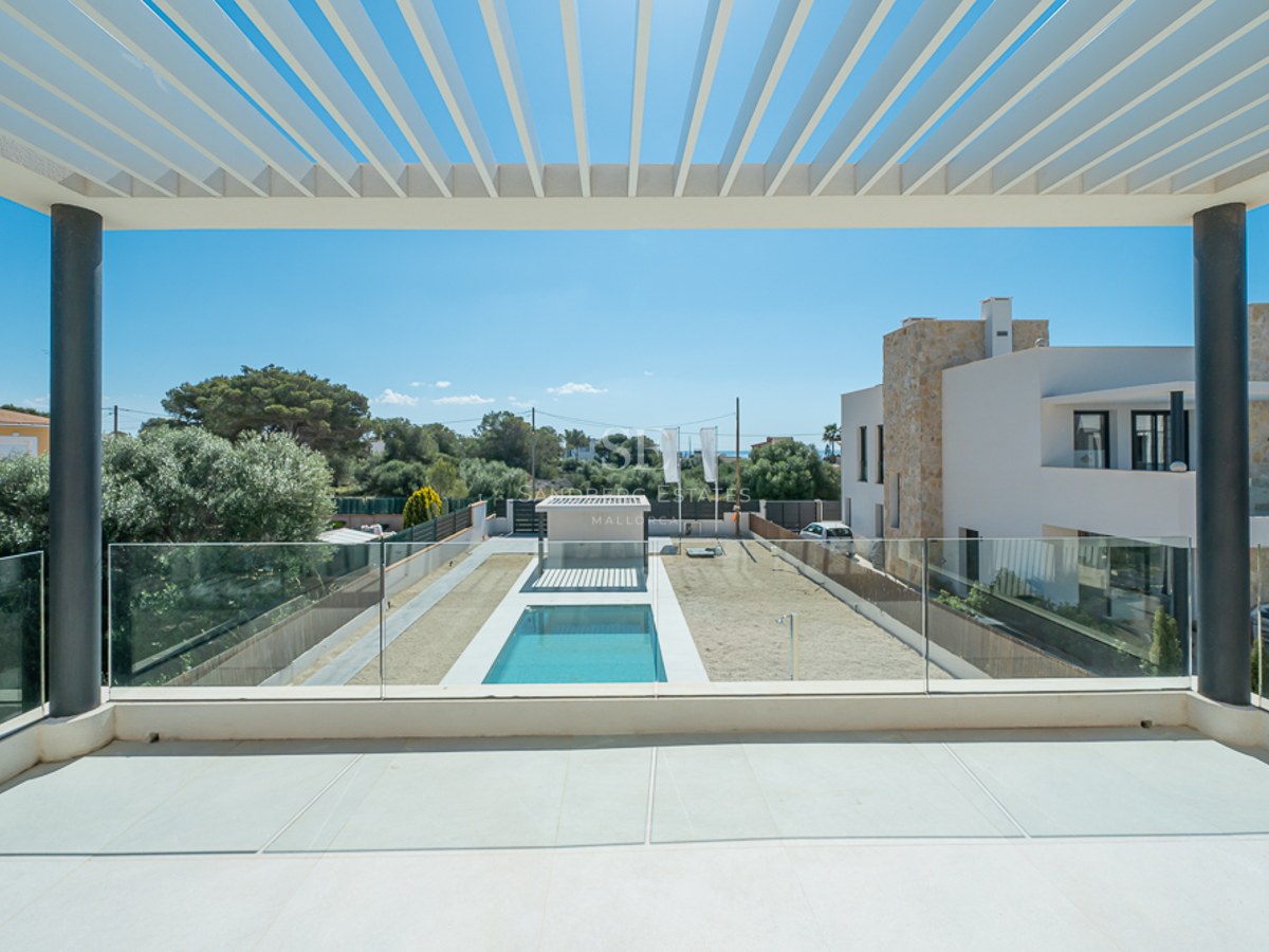 Vue depuis un balcon moderne avec pergola blanche et garde-corps en verre donnant sur une piscine et un jardin.