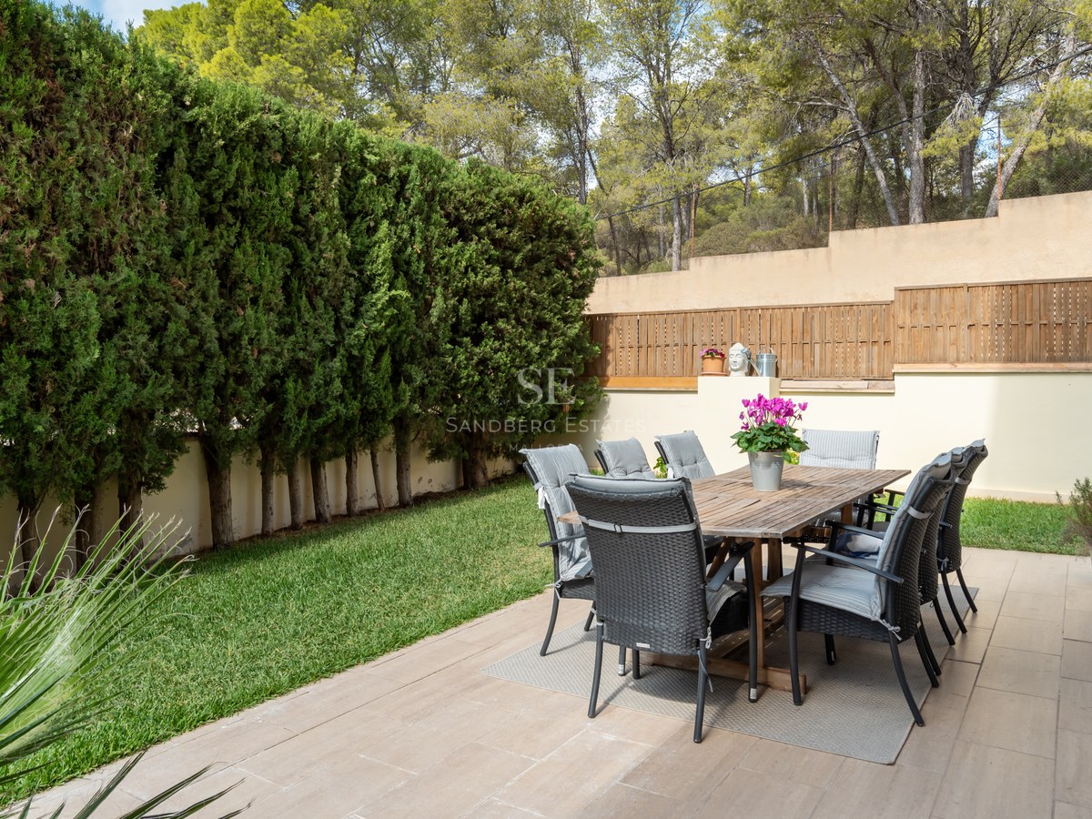 Mesa de madera y ocho sillas en terraza rodeada de altos setos de ciprés y jardín.