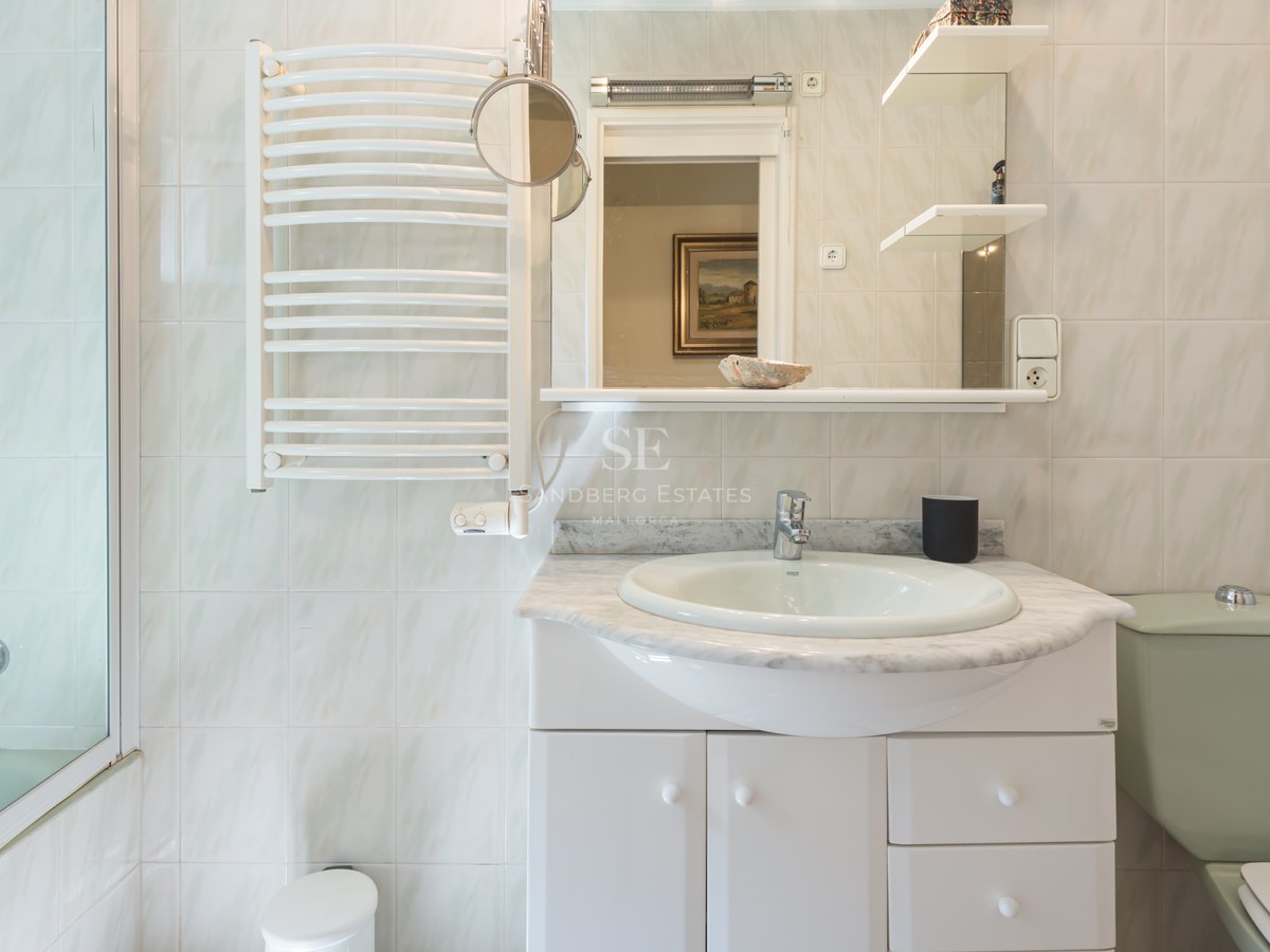 Salle de bains avec meuble blanc, plan en marbre gris, miroir, sèche-serviettes et carrelage mural clair.