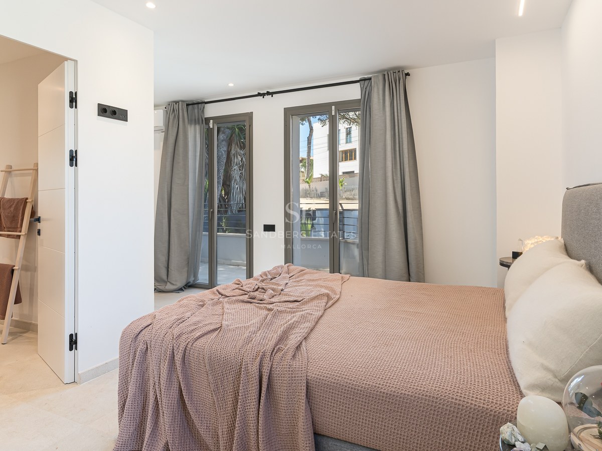 Modernes Schlafzimmer mit gepolstertem Bett, bodentiefen Fenstern und integriertem Badzugang.