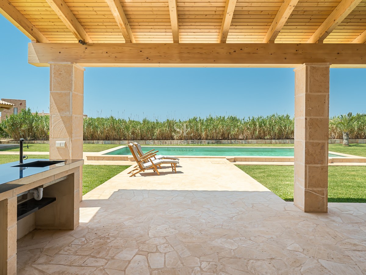 View from a stone-covered terrace with an outdoor kitchen looking towards a swimming pool and garden.