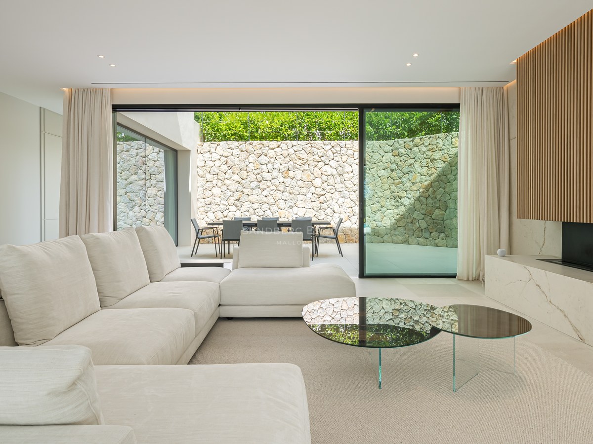 Zeitgenössisches Wohnzimmer mit großem weißen Ecksofa, Marmorkamin und Glastüren zu einer Terrasse mit Natursteinmauer.