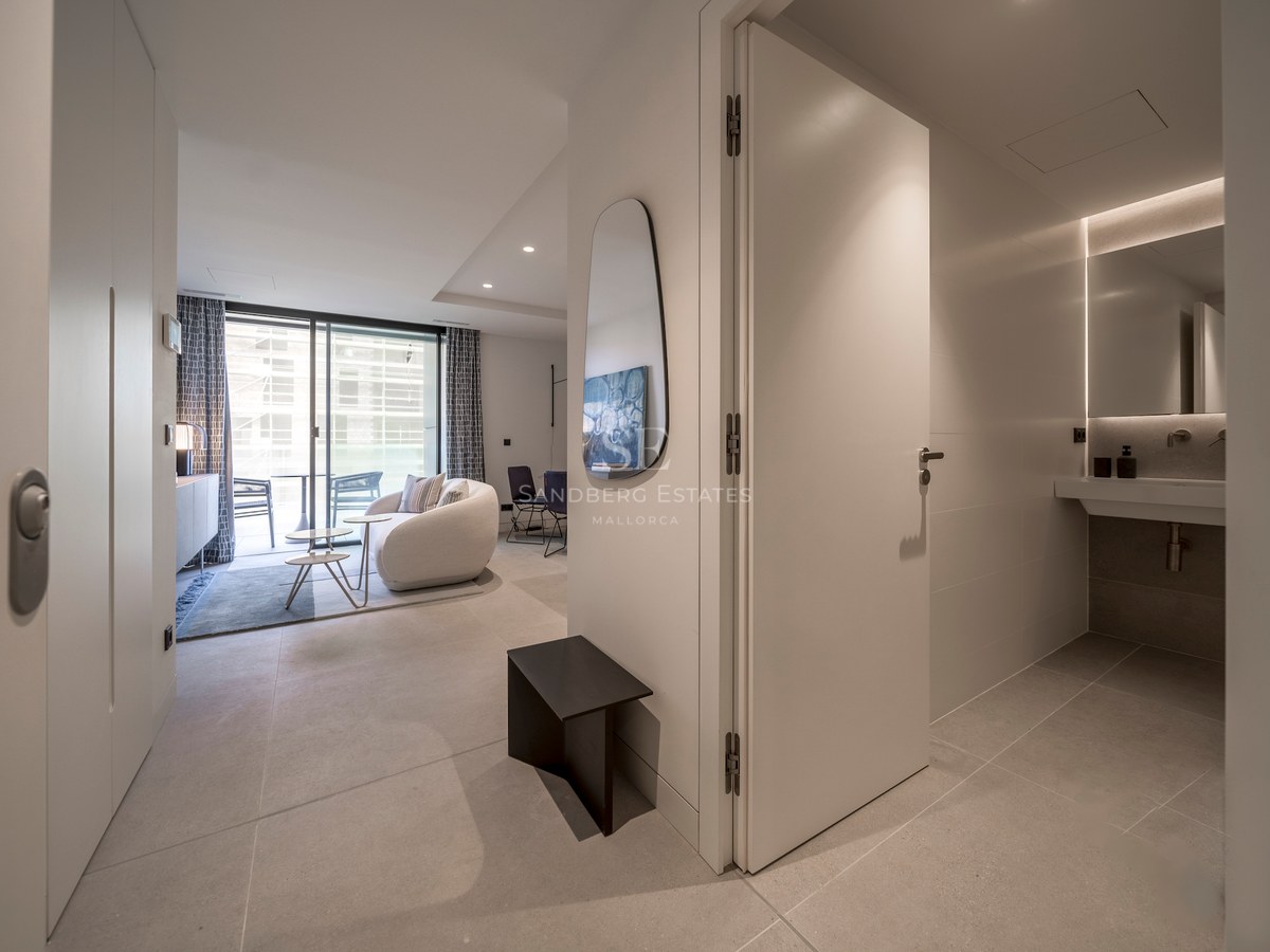 Couloir moderne menant à un salon lumineux avec canapé incurvé et une salle de bain chic sur la droite.