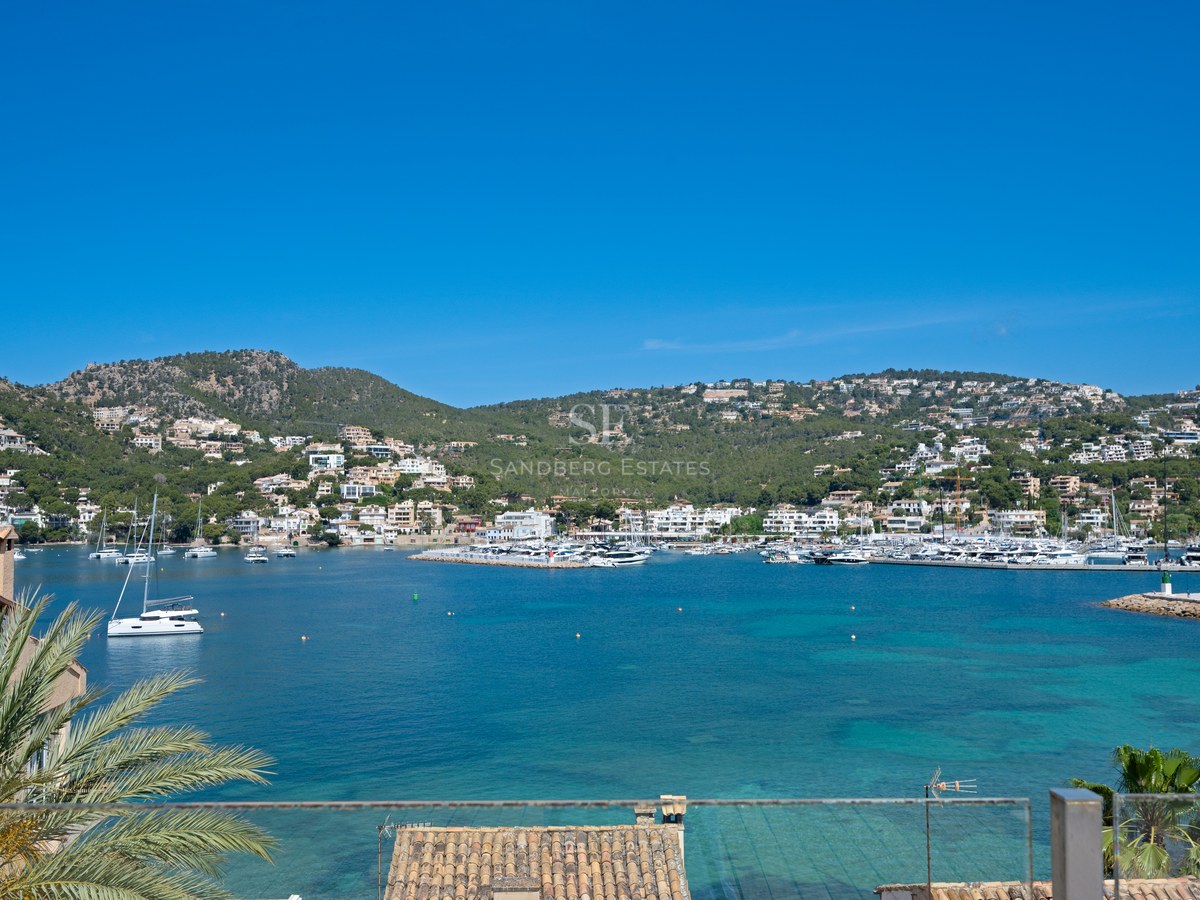 High-angle view of a turquoise Mediterranean harbor filled with yachts, surrounded by lush green hills and white villas.