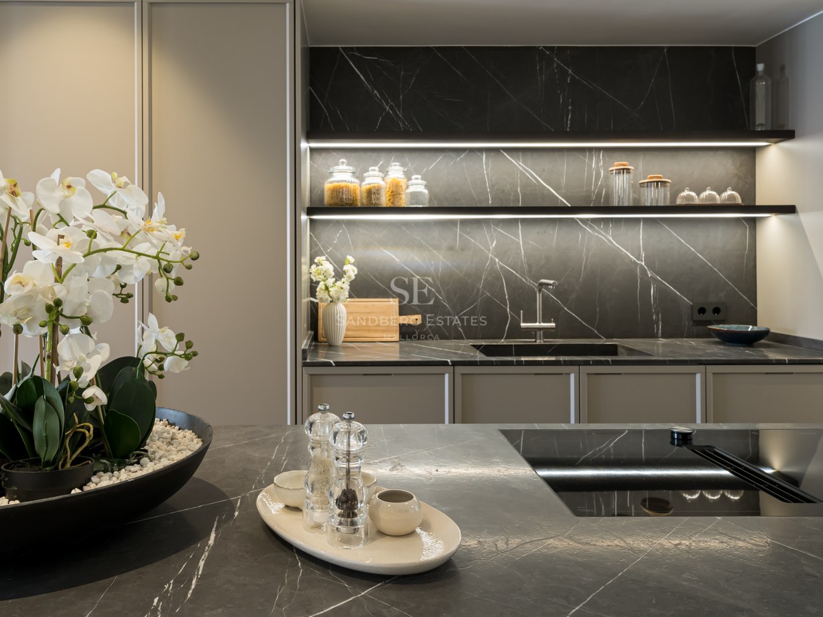 Cocina moderna con encimeras de mármol oscuro, electrodomésticos integrados e iluminación LED en estanterías.