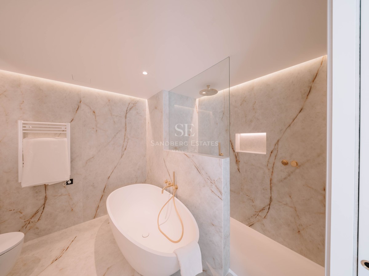 Salle de bain élégante avec baignoire îlot, douche à l'italienne et murs en marbre avec robinetterie dorée.