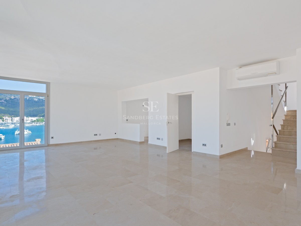 Empty bright living room with polished marble floors and a glass door overlooking a marina with yachts.