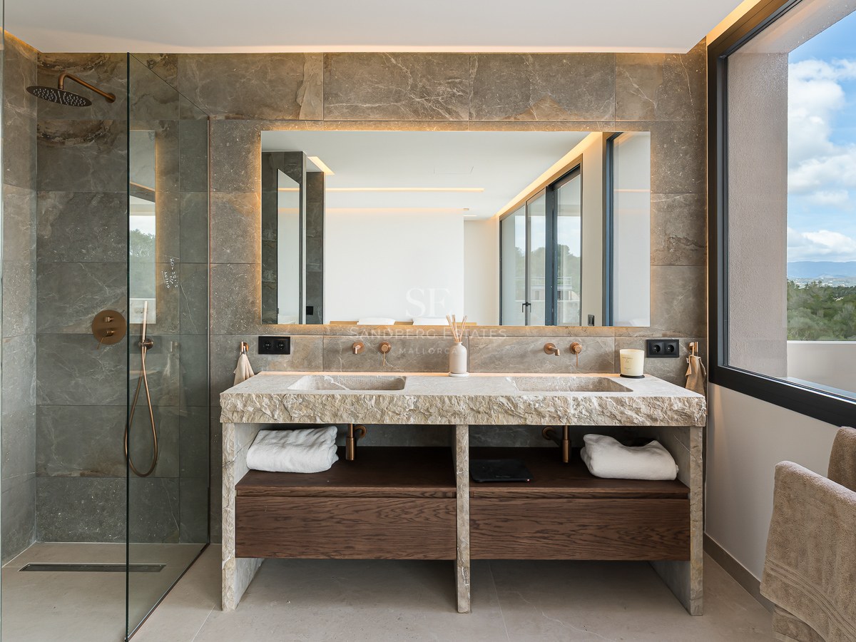 Luxury bathroom featuring a double natural stone vanity, large backlit mirror, glass shower, and dark wood cabinetry.