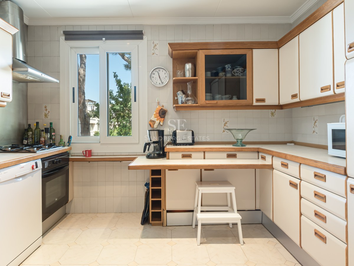 Cuisine claire avec placards blancs, finitions en bois, plan de travail fonctionnel et fenêtre sur le jardin.
