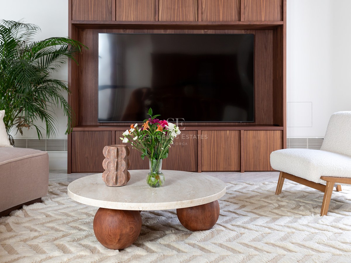 Contemporary living room featuring a walnut TV unit, round travertine coffee table, and white bouclé armchair.