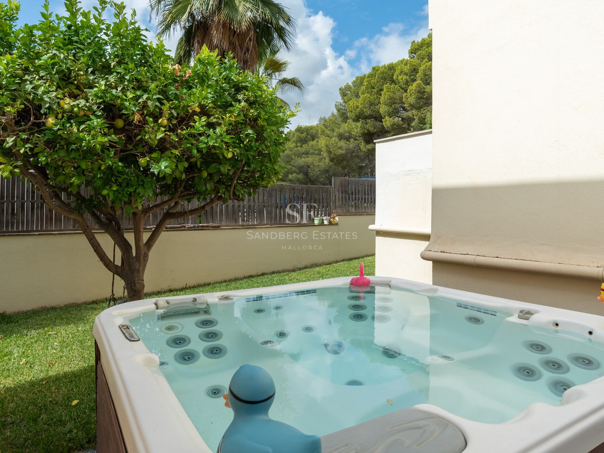 Un jacuzzi exterior moderno en un entorno de jardín privado junto a un limonero y una pared blanca.