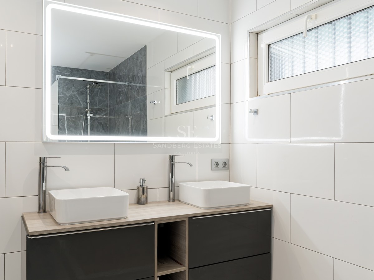 Modern bathroom featuring a double vanity with square sinks, a large LED backlit mirror, and white tiled walls.