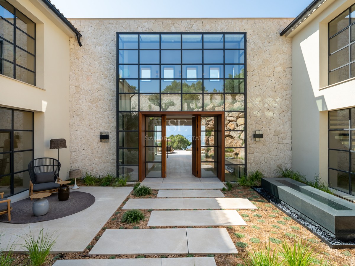 Main entrance of a luxury villa featuring natural stone walls, expansive glass windows, and a massive wooden pivot door.