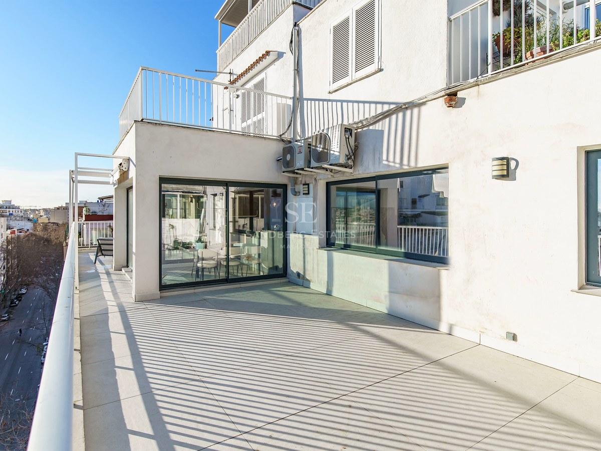 Terrasse ensoleillée avec carrelage clair, garde-corps blancs et vue sur une rue citadine sous un ciel bleu.