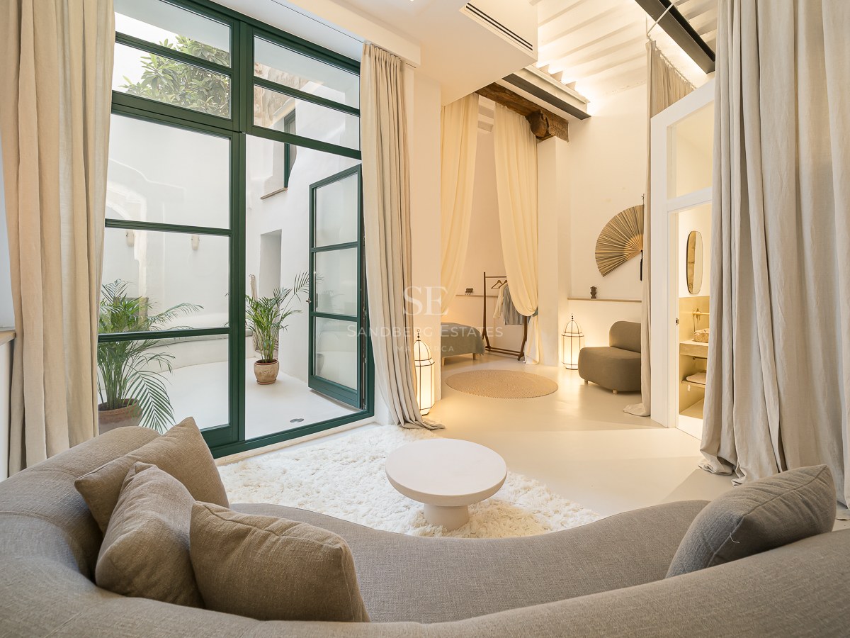 Salon moderne avec un canapé gris incurvé, un tapis à poils longs et de grandes portes vitrées ouvrant sur un patio.