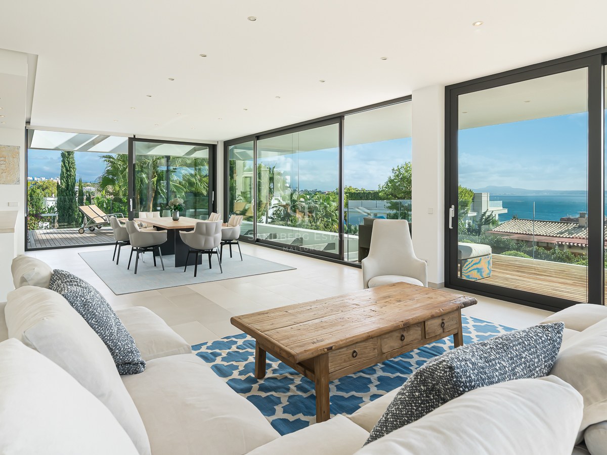 Salon spacieux avec canapés blancs, table basse en bois et grandes baies vitrées s'ouvrant sur une terrasse vue mer.