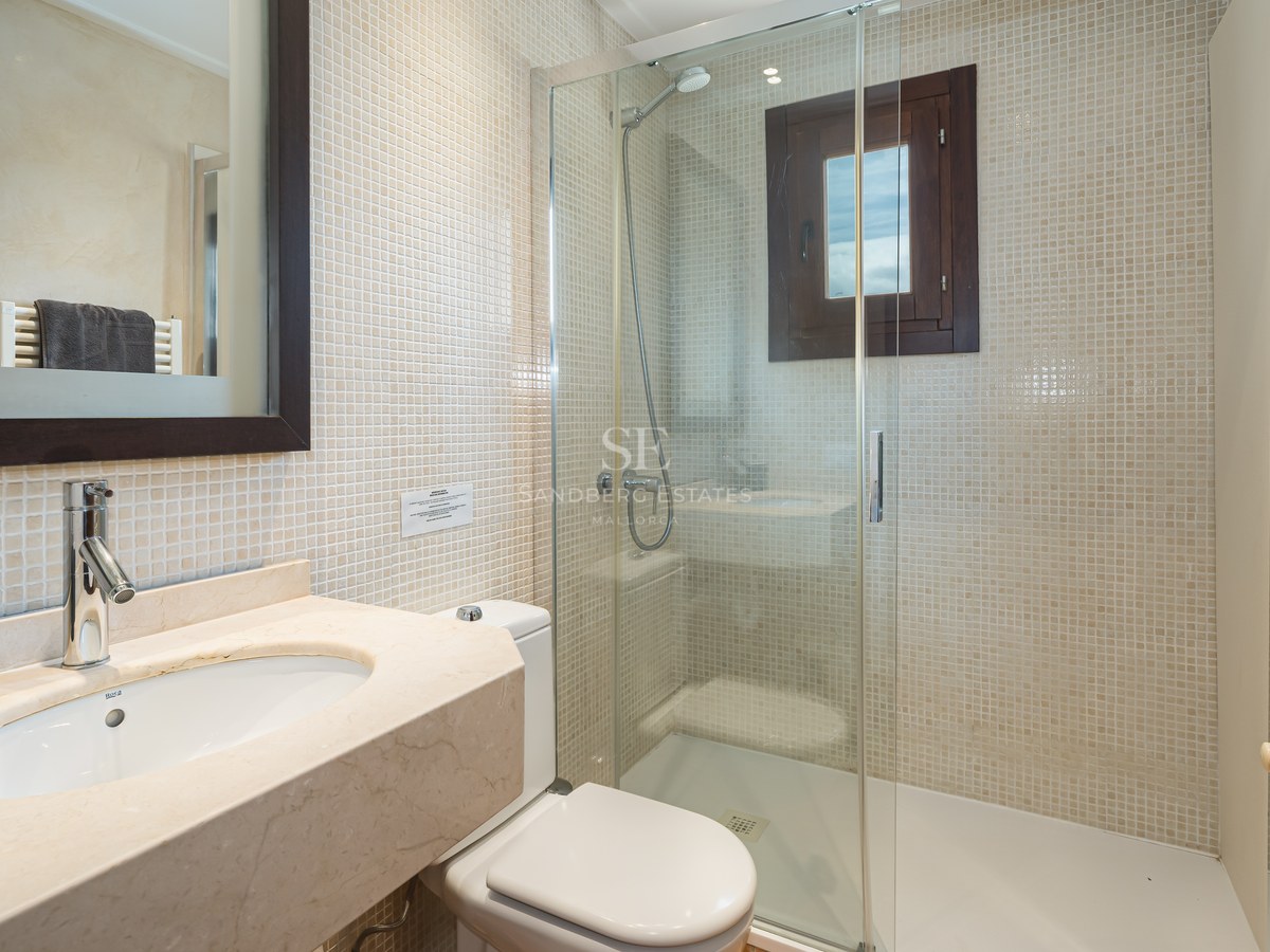 Badrum med glasdusch, beige mosaikväggar och tvättställ i marmor under en mörk spegelram.