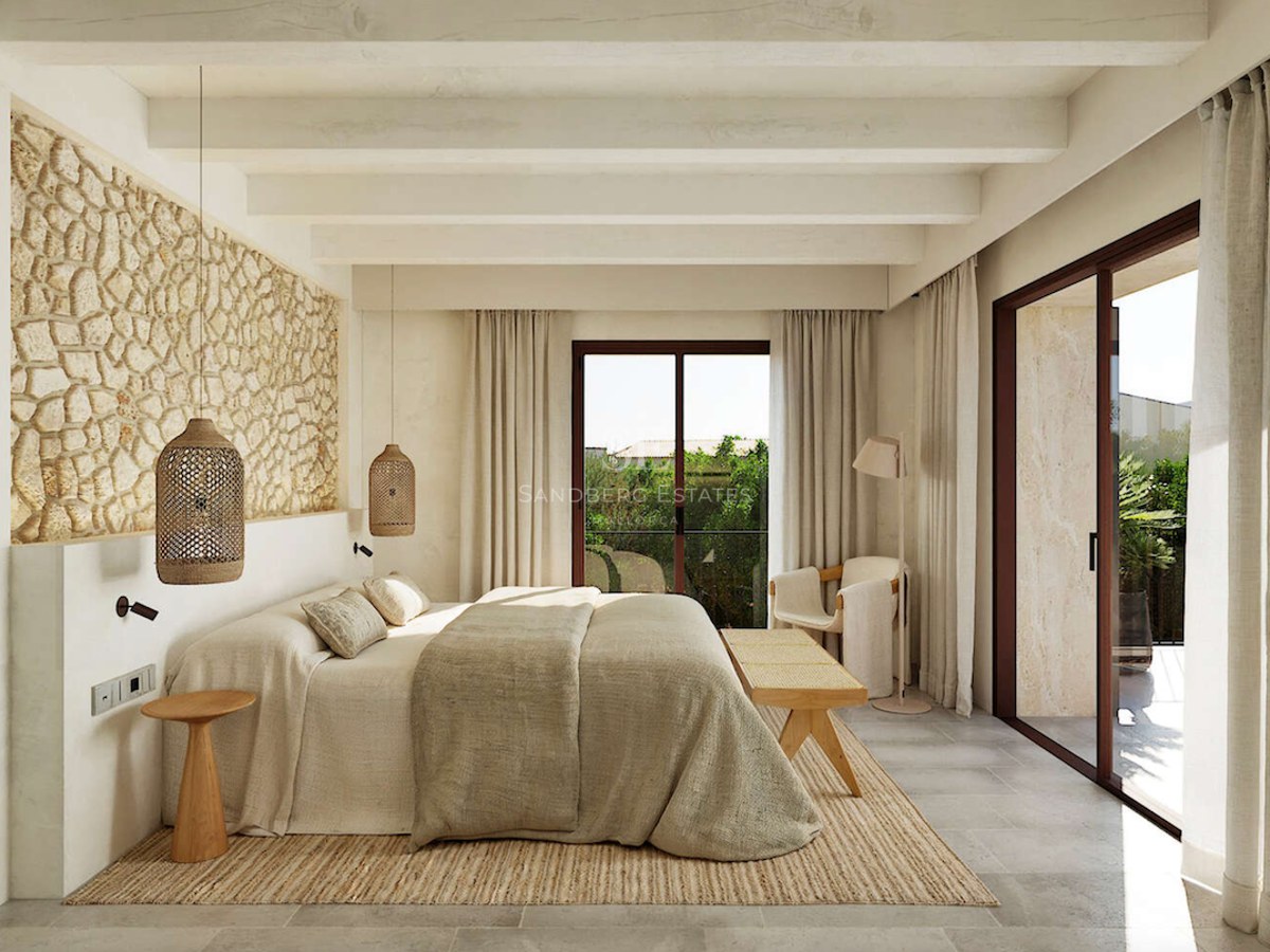 Chambre de luxe avec mur en pierre apparente, poutres en bois et baies vitrées donnant sur le jardin.