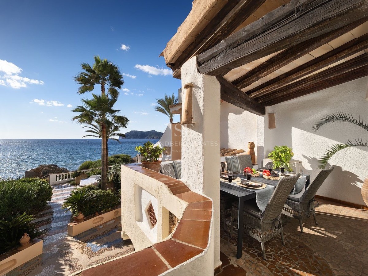 Terrasse couverte avec poutres en bois, table à manger, chaises en osier et vue imprenable sur la mer et les palmiers.