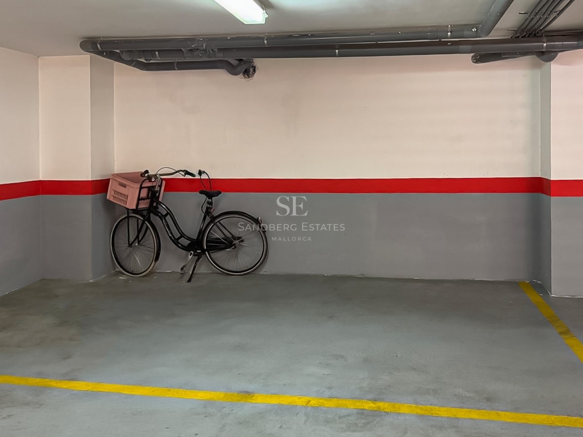 Place de parking numérotée avec murs gris et blancs, bande rouge et sol en béton avec lignes jaunes.