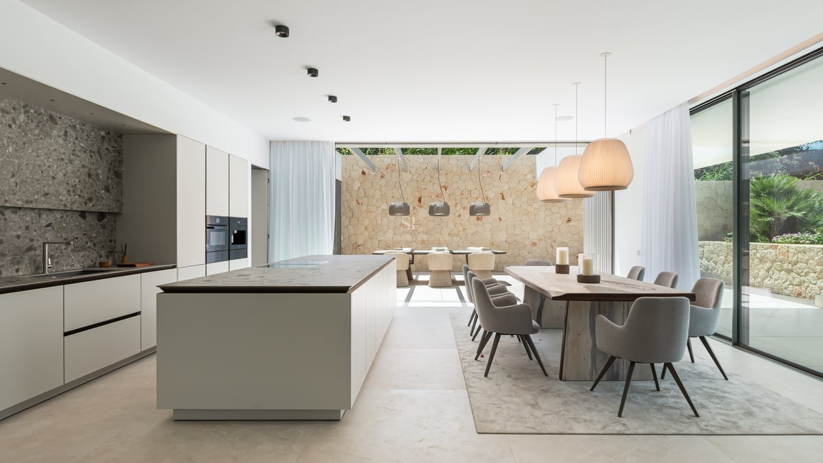 Cuisine contemporaine avec îlot en marbre et salle à manger s'ouvrant sur un patio ensoleillé avec mur en pierre.
