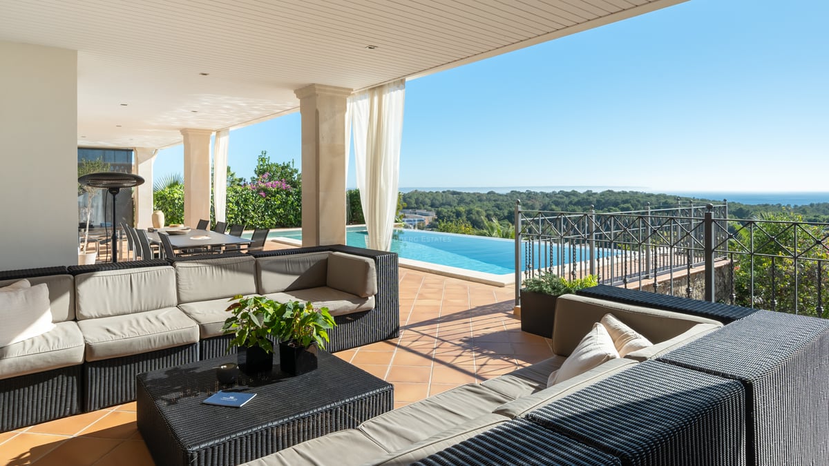 Terrasse de luxe ombragée avec canapés en osier, sol en terre cuite et piscine à débordement sur la mer.