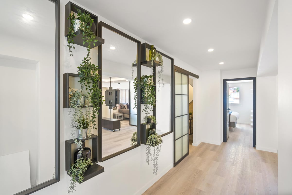 Couloir moderne avec miroirs à cadre noir, étagères intégrées avec plantes et parquet en bois clair.