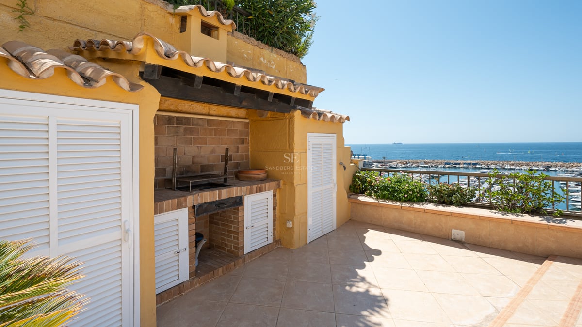 Terrasse extérieure avec barbecue en briques, murs jaunes et vue sur un port de plaisance et l'océan.