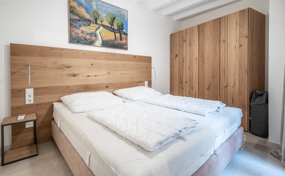 Chambre avec grande armoire en chêne, tête de lit en bois intégrée et lit double avec draps blancs.