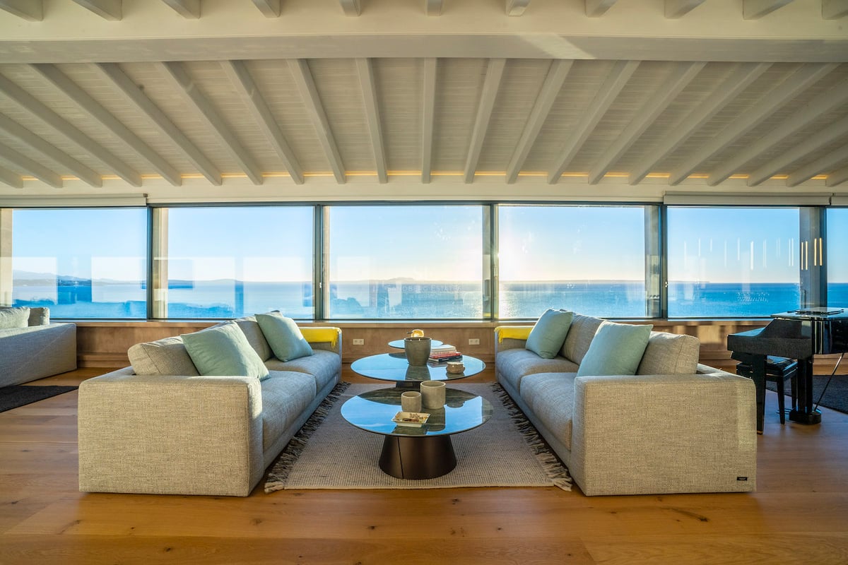 Salon moderne avec canapés gris, tables basses en verre et baies vitrées donnant sur la mer Méditerranée.