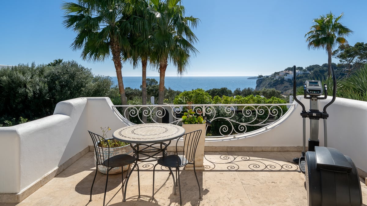 Terrasse blanche avec mobilier en fer et elliptique offrant une vue sur les palmiers et la mer Méditerranée.