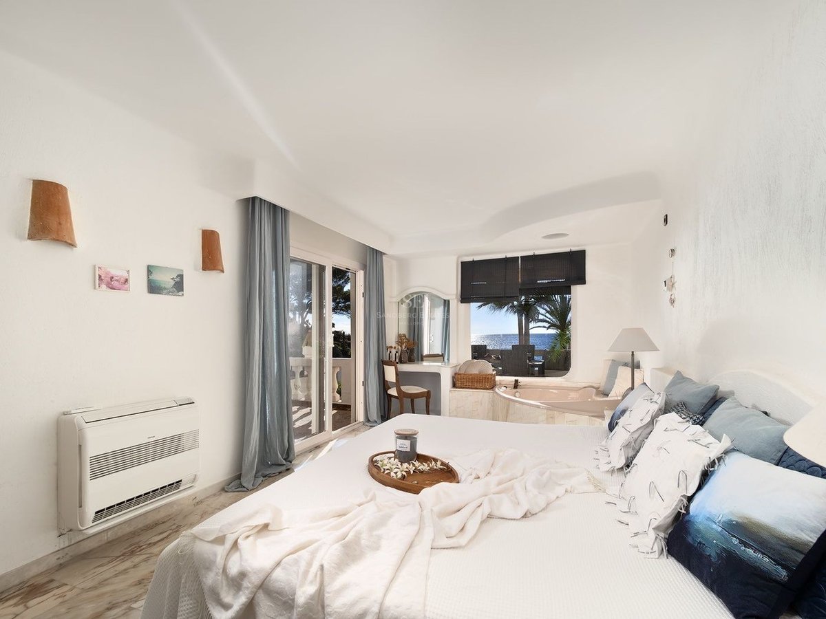 Chambre principale blanche et lumineuse avec baignoire intégrée près de la fenêtre et balcon vue mer.