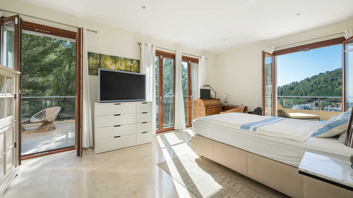 Chambre ensoleillée avec sol en marbre, lit double et portes vitrées ouvrant sur un balcon avec vue sur les collines.
