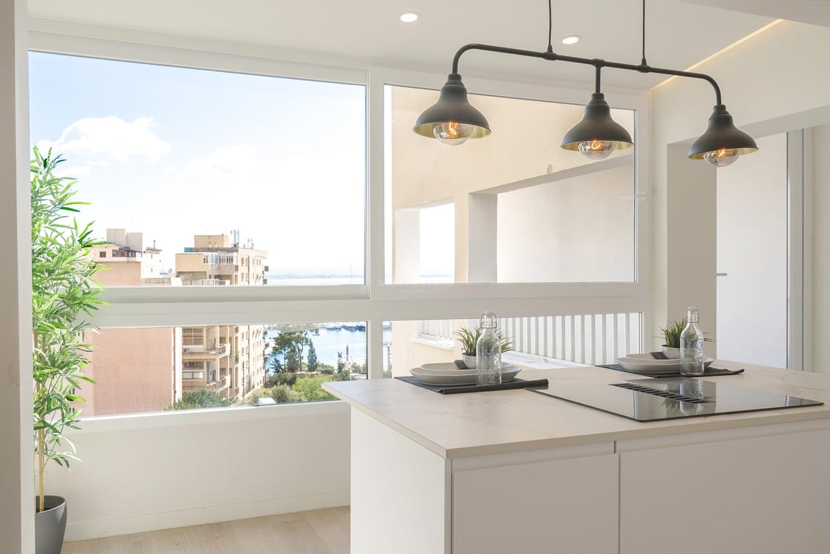 Îlot de cuisine blanc avec plaque de cuisson devant une fenêtre offrant une vue sur le port et la ville.