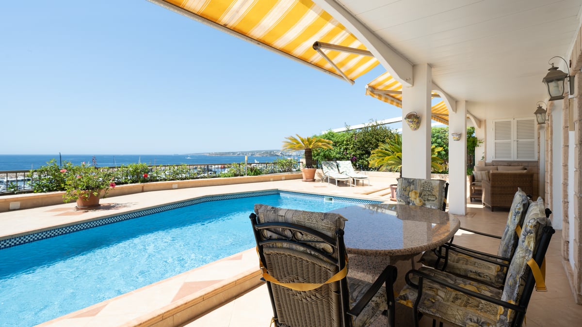 Terrasse avec piscine bleue, coin repas extérieur et stores jaunes offrant une vue imprenable sur la mer.