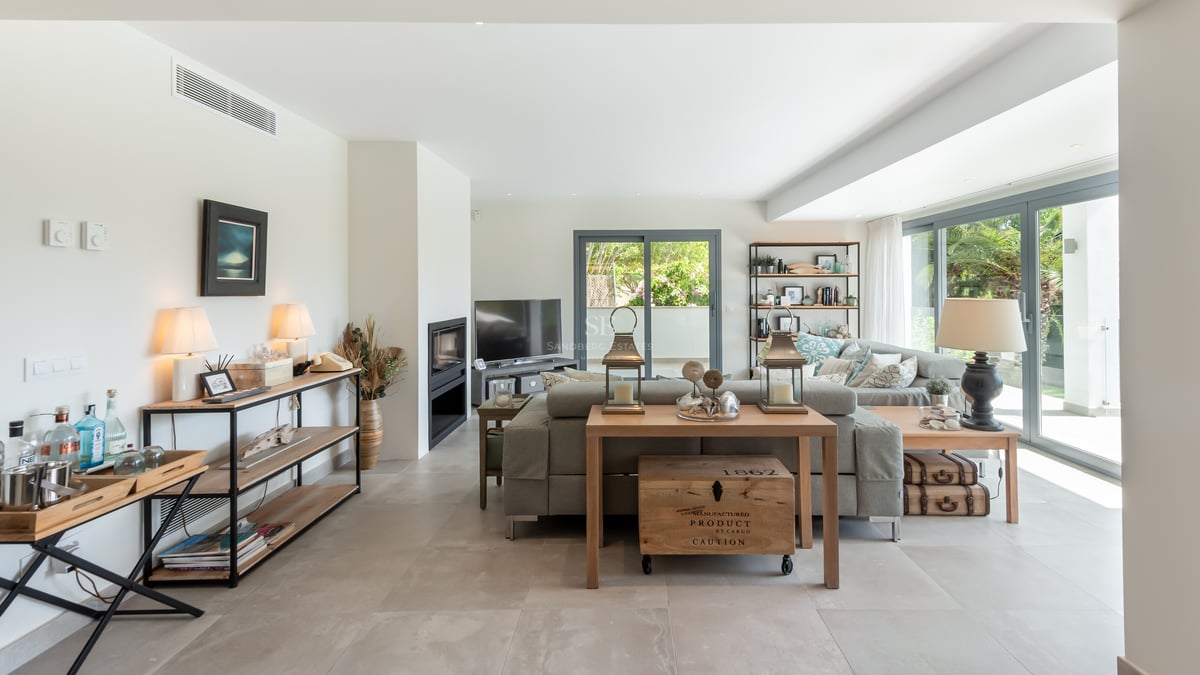 Grand salon moderne avec canapé gris, baies vitrées donnant sur le jardin, sol en grès et cheminée intégrée.