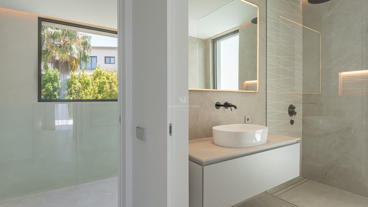 Salle de bains moderne avec vasque à poser, robinetterie noir mat et douche à l'italienne à côté d'une fenêtre vue jardin.