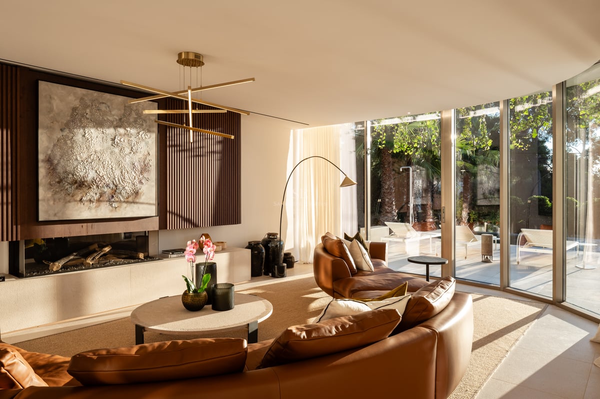 Salon moderne avec canapé en cuir courbé, cheminée linéaire et baies vitrées donnant sur le jardin.