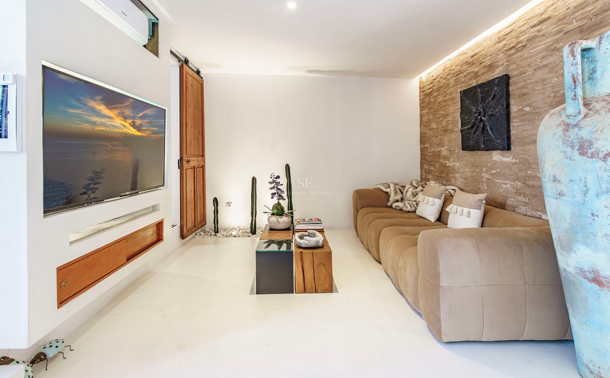 Salon avec canapé beige, mur en pierre rustique, télévision encastrée et décoration méditerranéenne.