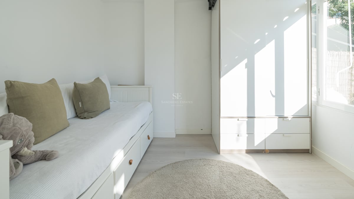 Chambre blanche avec lit gigogne, coussins vert olive, grande armoire et tapis rond gris.